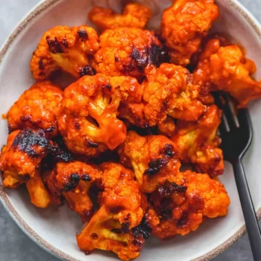 Plate of easy Buffalo Cauliflower with spicy sauce and fresh vegetables
