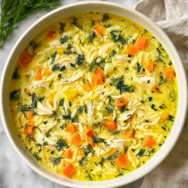 Bowl of Greek Lemon Chicken Soup garnished with fresh herbs and lemon wedges.