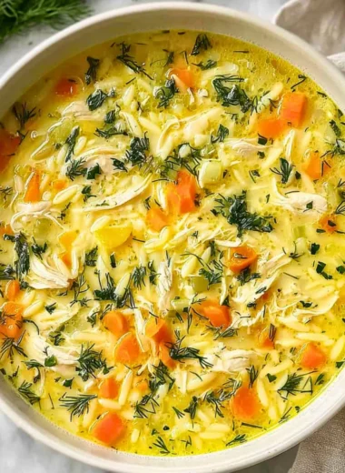 Bowl of Greek Lemon Chicken Soup garnished with fresh herbs and lemon wedges.