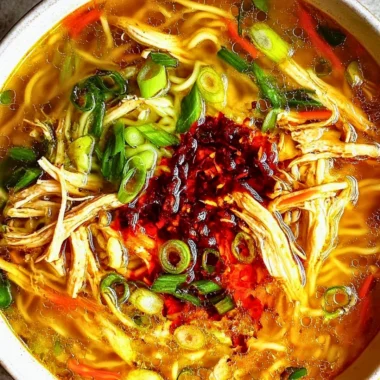 Bowl of classic ginger garlic chicken noodle soup garnished with herbs.