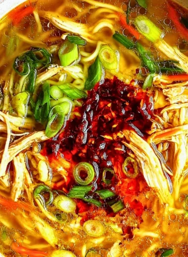 Bowl of classic ginger garlic chicken noodle soup garnished with herbs.