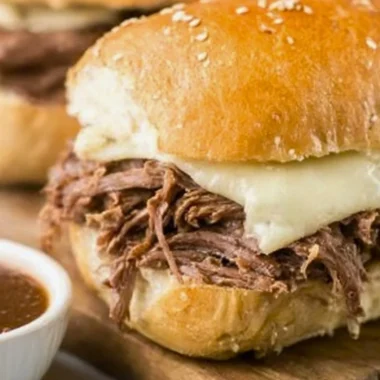 Crock Pot French Dip sandwich with juicy meat and dipping sauce on a wooden board