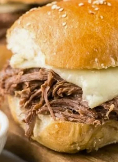 Crock Pot French Dip sandwich with juicy meat and dipping sauce on a wooden board