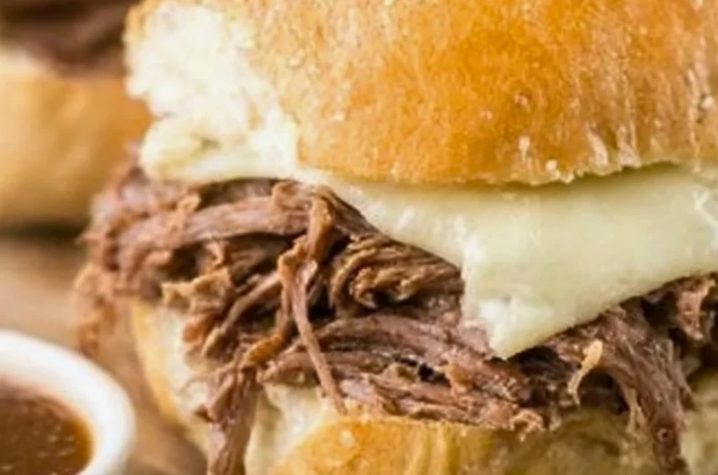 Crock Pot French Dip sandwich with juicy meat and dipping sauce on a wooden board