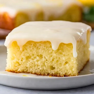 Delicious homemade lemonade poke cake with lemon icing on a serving plate.
