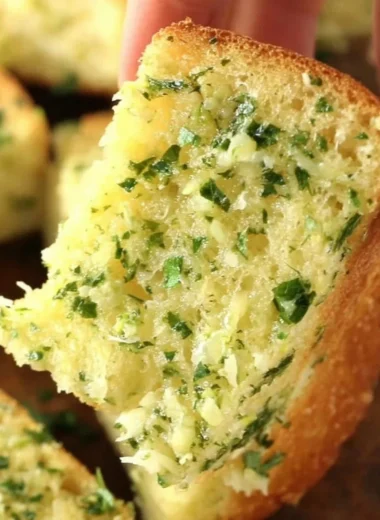 Sliced homemade garlic bread with herbs and butter on a wooden board
