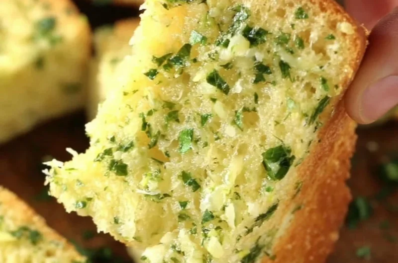 Sliced homemade garlic bread with herbs and butter on a wooden board