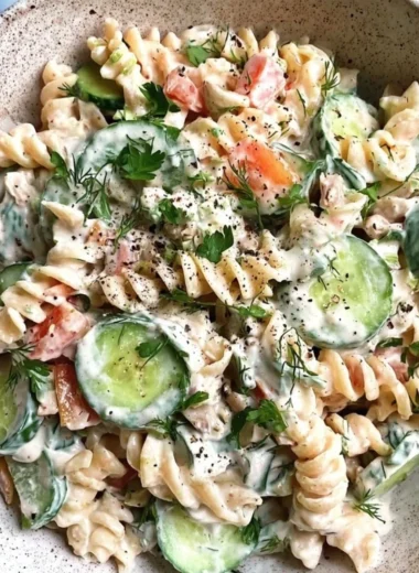 A vibrant bowl of Tzatziki Pasta Salad topped with fresh herbs and vegetables.